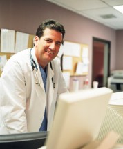 Male HCP with stethoscope and lab coat viewing a computer